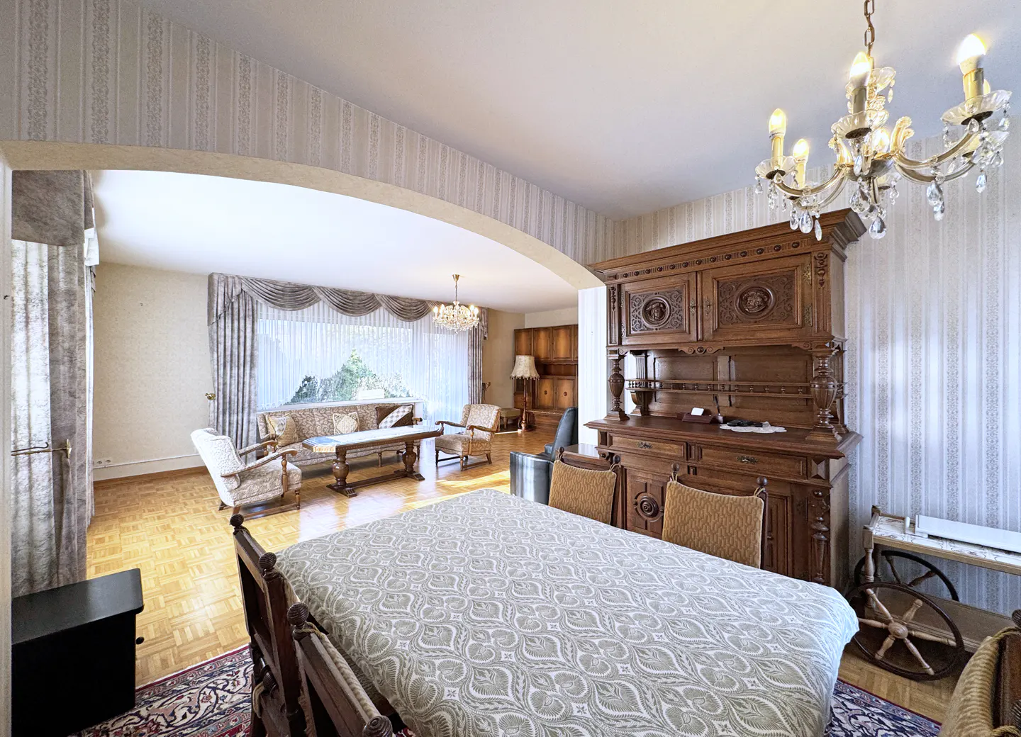A bright living room with a dining table, a wooden hutch, and a chandelier.