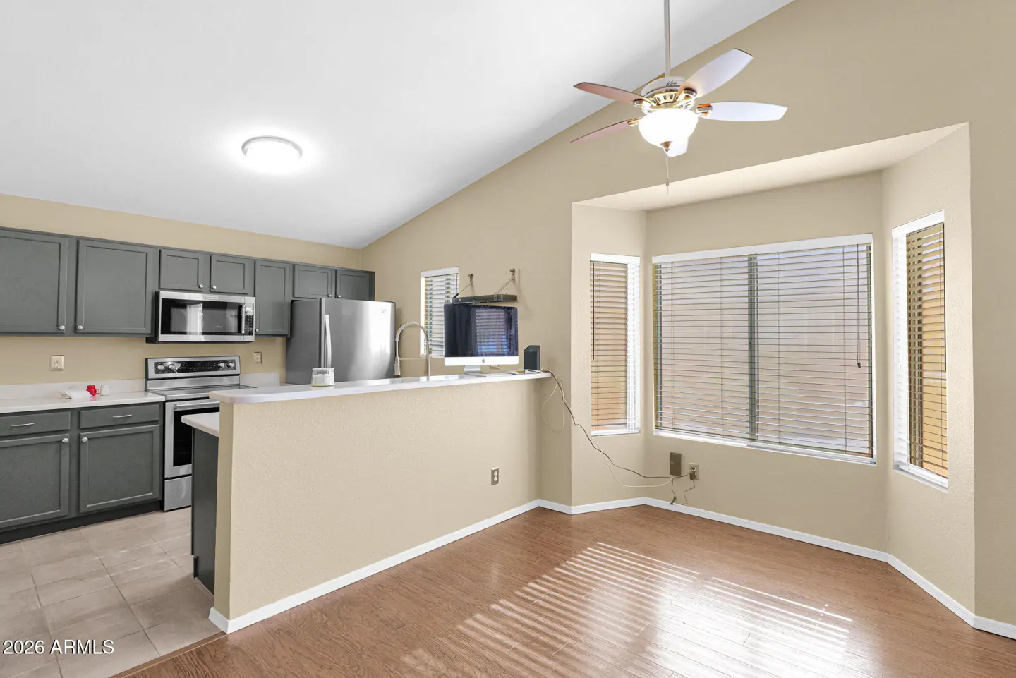 A kitchen with gray cabinets, stainless steel appliances, and a breakfast nook with large windows.