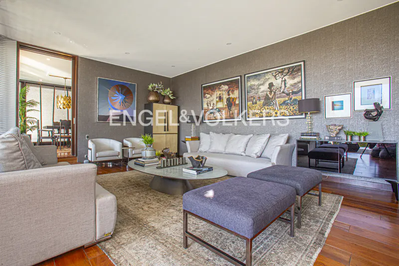 Living room with gray walls, wood floors, and a patterned rug. Sofas, chairs, and art are visible. Engel & Volkers logo is superimposed.