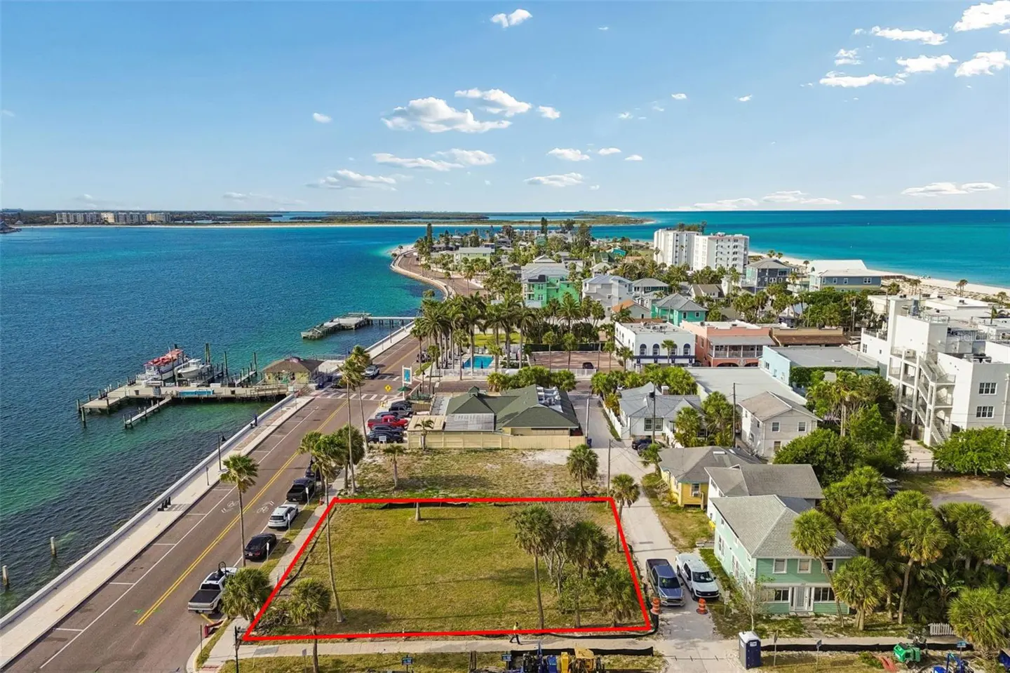Aerial view of a vacant lot outlined in red, near a pier and colorful buildings, under a blue sky.