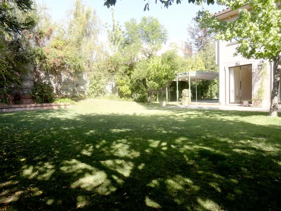 A large green lawn with tree shadows leads to a house and covered patio.