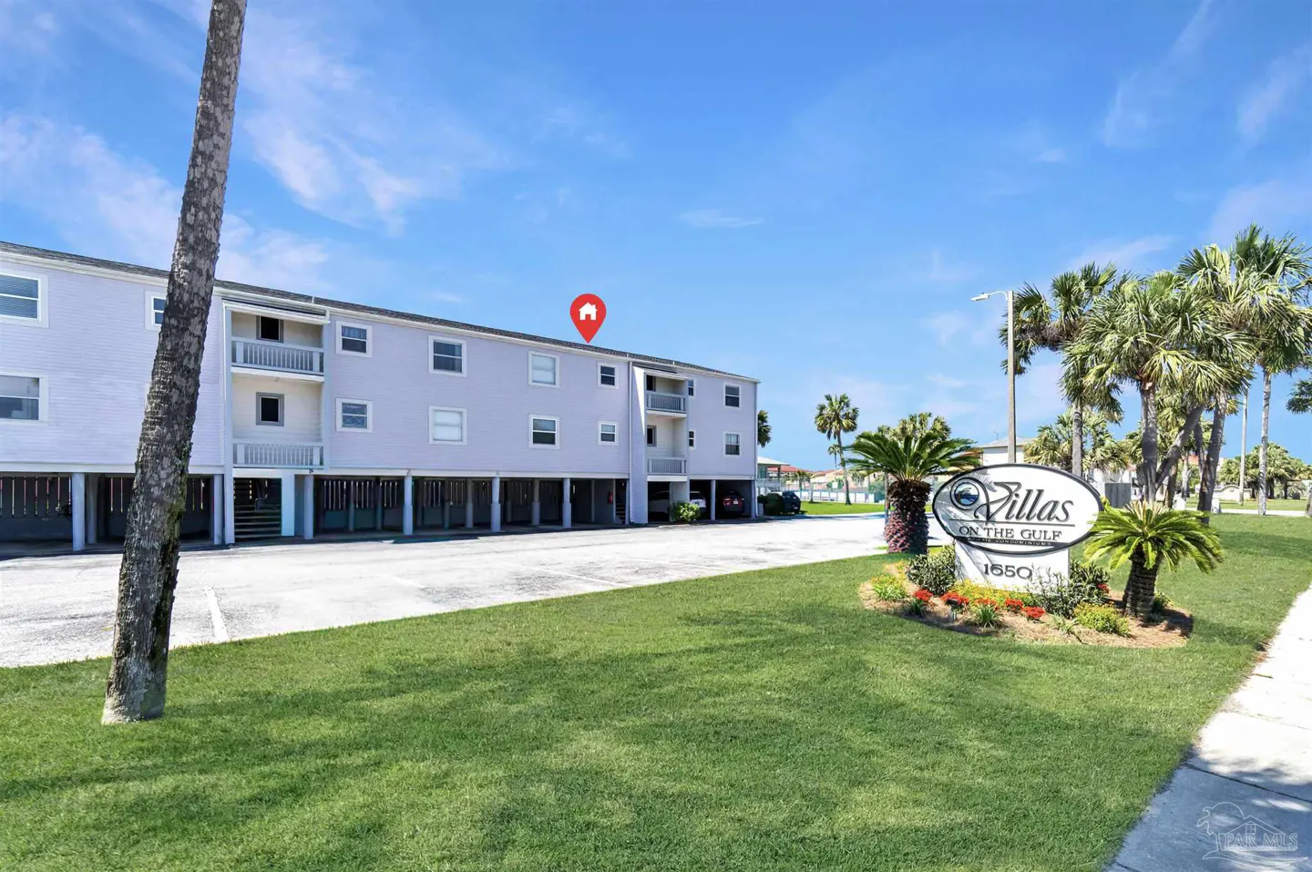 Exterior of "Villas on the Gulf," a light purple, multi-story building on stilts, with a sign and palm trees.