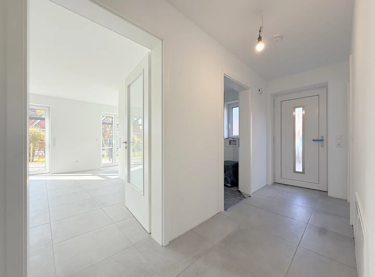 Bright, modern home interior with white walls, gray tile floors, and white doors. A living room is visible through an open doorway.