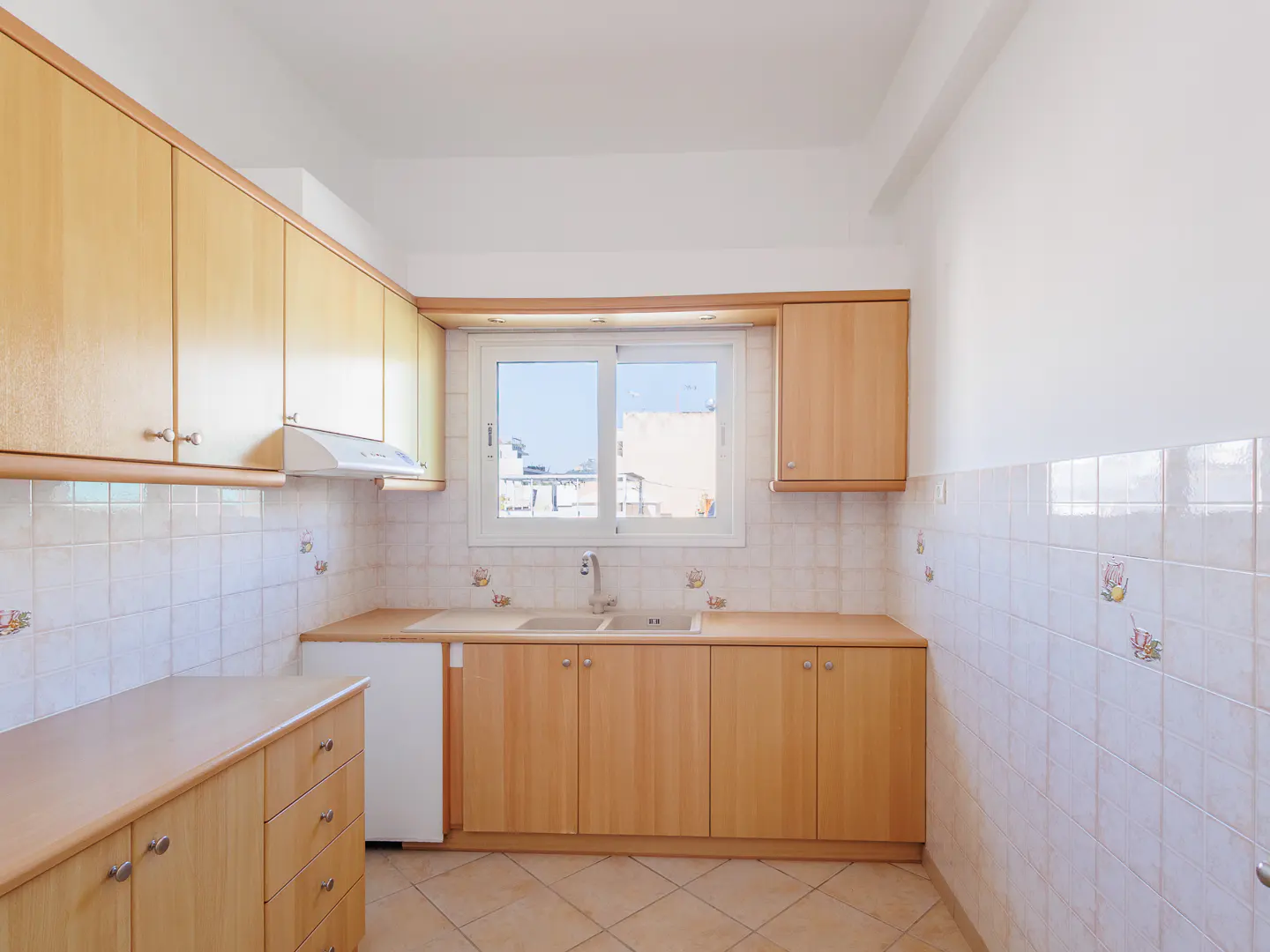 Bright kitchen with light wood cabinets, white walls and tiled backsplash. A window above the sink offers a view of the outside.