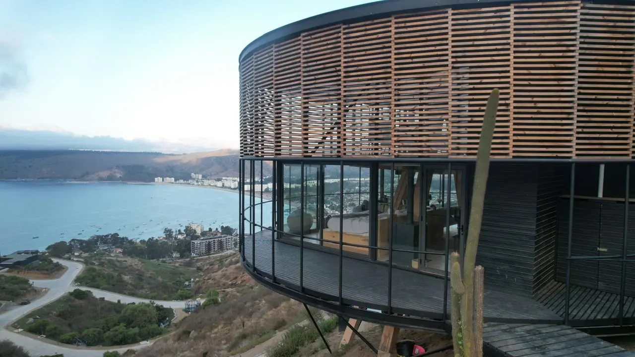 Modern round house with wood slats and glass walls overlooking a bay and town on a hill.