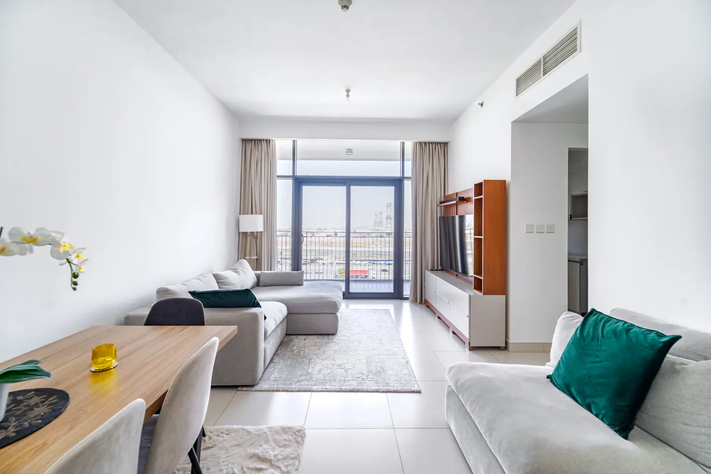 Bright living room with white walls, a gray sectional sofa, a wood dining table, and a balcony with a city view.