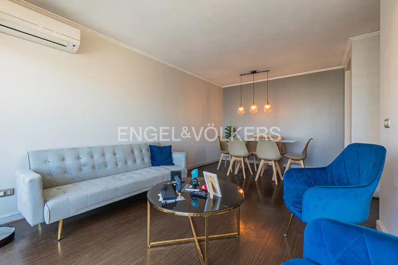 Living room with a light gray sofa, blue chairs, and a round coffee table. Dining table with chairs in the background.