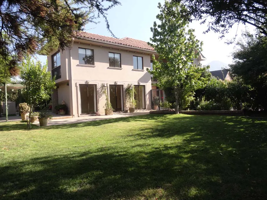 Two-story beige house with a red tile roof and a large green lawn. Trees frame the house.