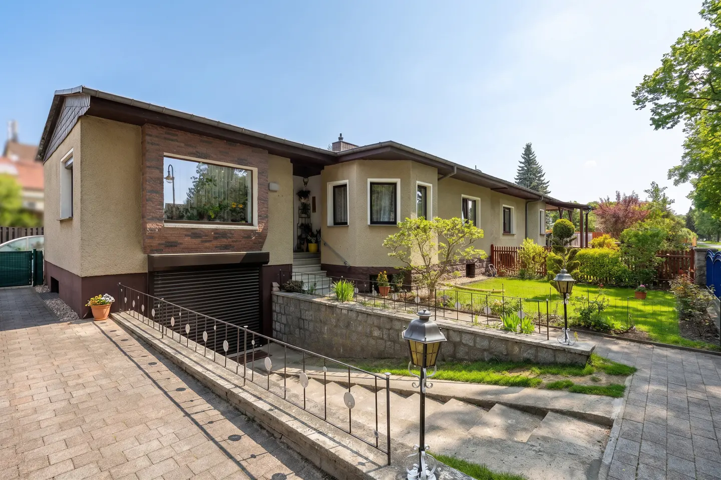 A one-story beige house with a brown roof and trim, a garage, and a well-manicured lawn on a sunny day.