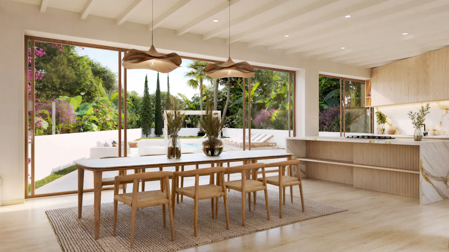 Bright dining room with a long table, wooden chairs, and pendant lights. Large windows overlook a lush garden with a pool. Kitchen area visible in the background.