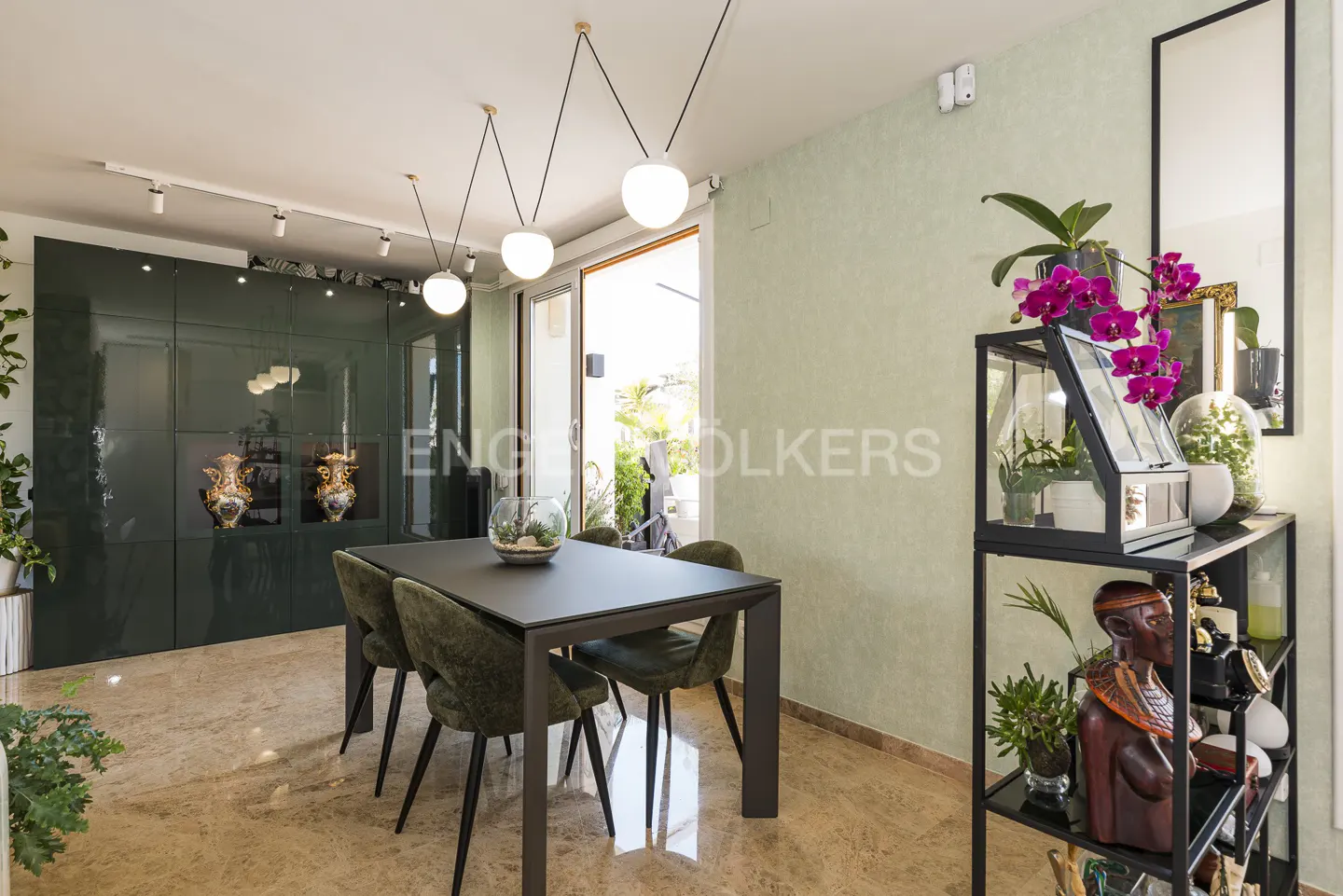 A dining room with a black table, green chairs, and a display cabinet with plants and decor.