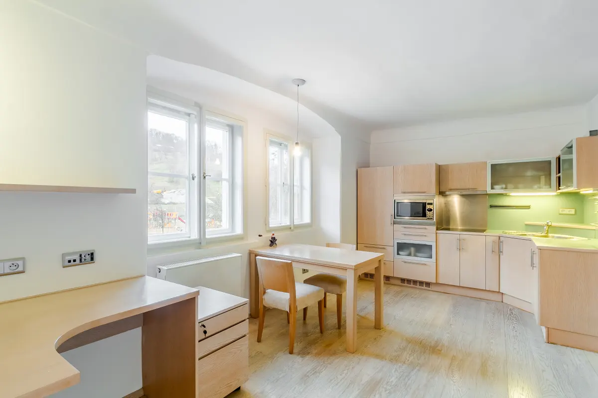 Bright, modern kitchen with light wood cabinets, a dining table with two chairs, and a desk area by the window.