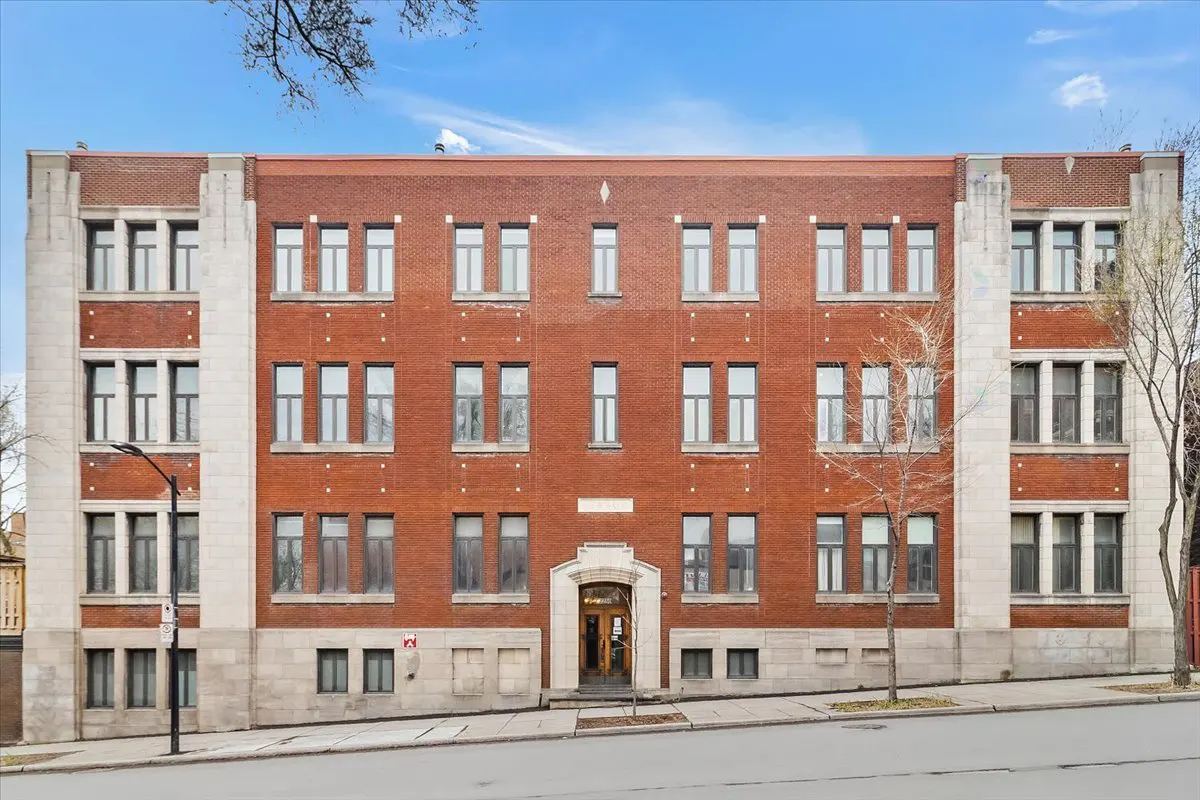 A four-story red brick apartment building with white stone accents under a blue sky.