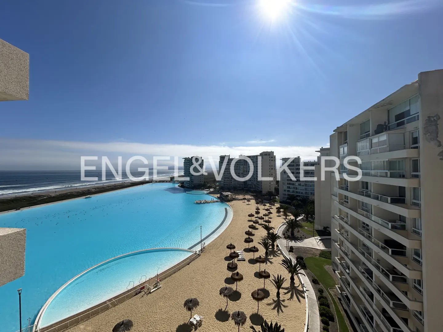 View from a high-rise of a turquoise lagoon, sandy beach with umbrellas, and ocean under a sunny blue sky.