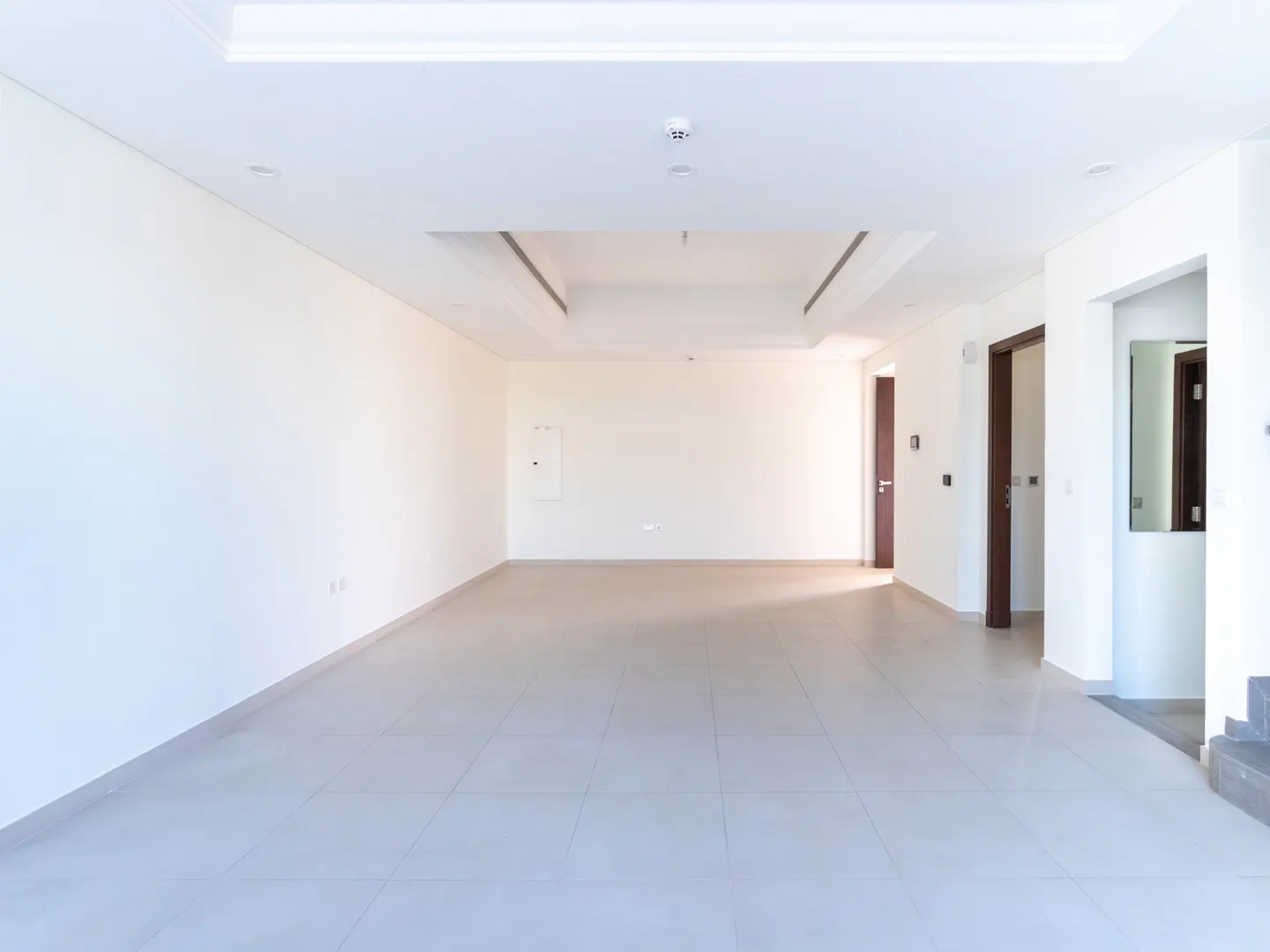 Bright, empty room with white walls, light gray tile floor, and recessed lighting. Two doorways are visible.