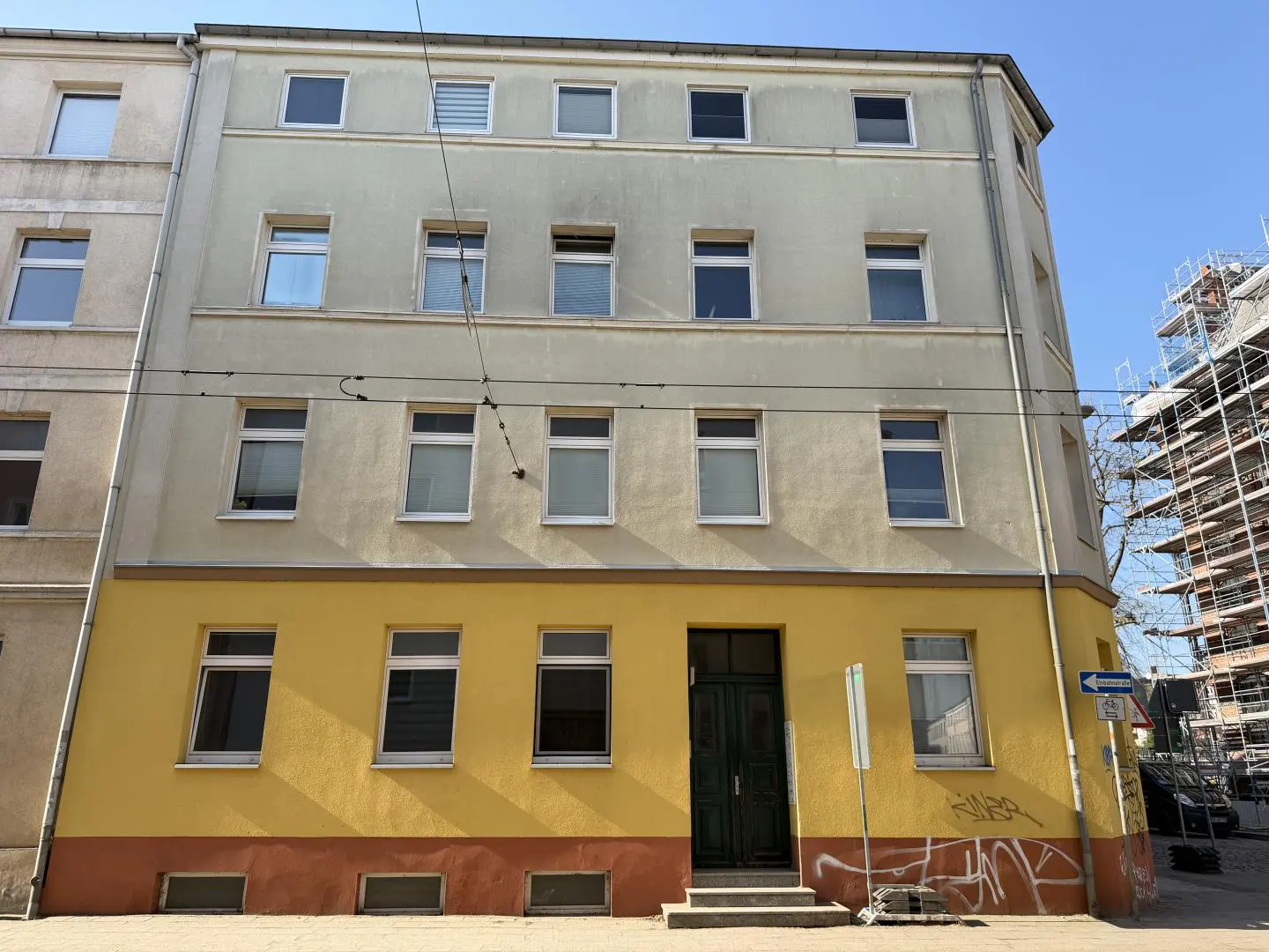 A three-story building with a yellow first floor and light gray upper floors, featuring many windows and a dark green door.