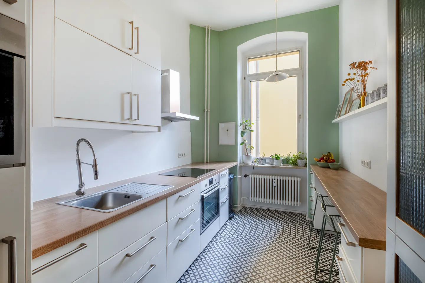 Bright kitchen with white cabinets, wood countertops, and black and white patterned floor. A large window overlooks a sunny view.