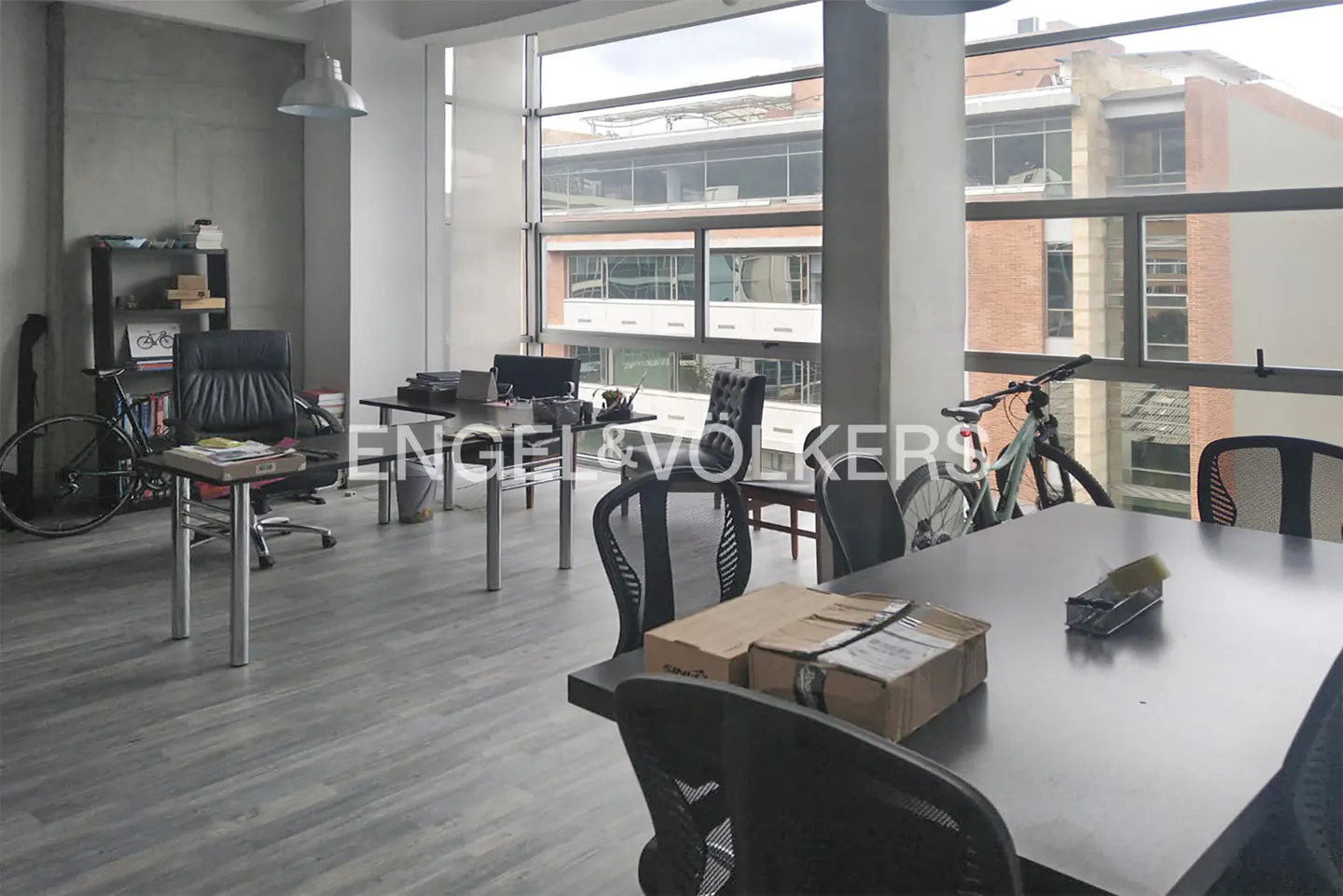 Bright office space with large windows, desks, chairs, and bicycles. Gray wood floors and concrete walls.