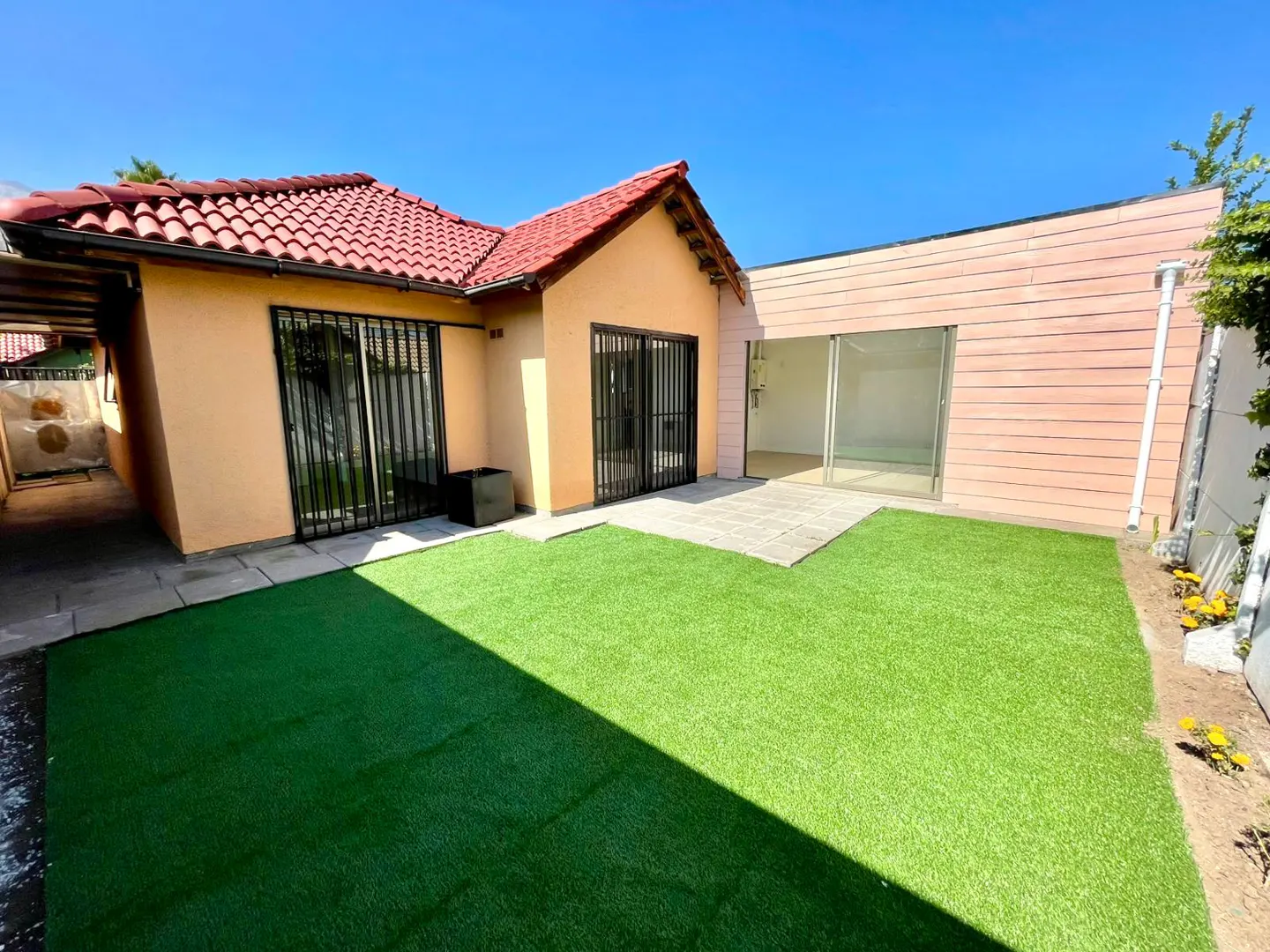 Backyard view of a single-story house with a red tile roof, peach walls, green lawn, and a pink-walled addition.