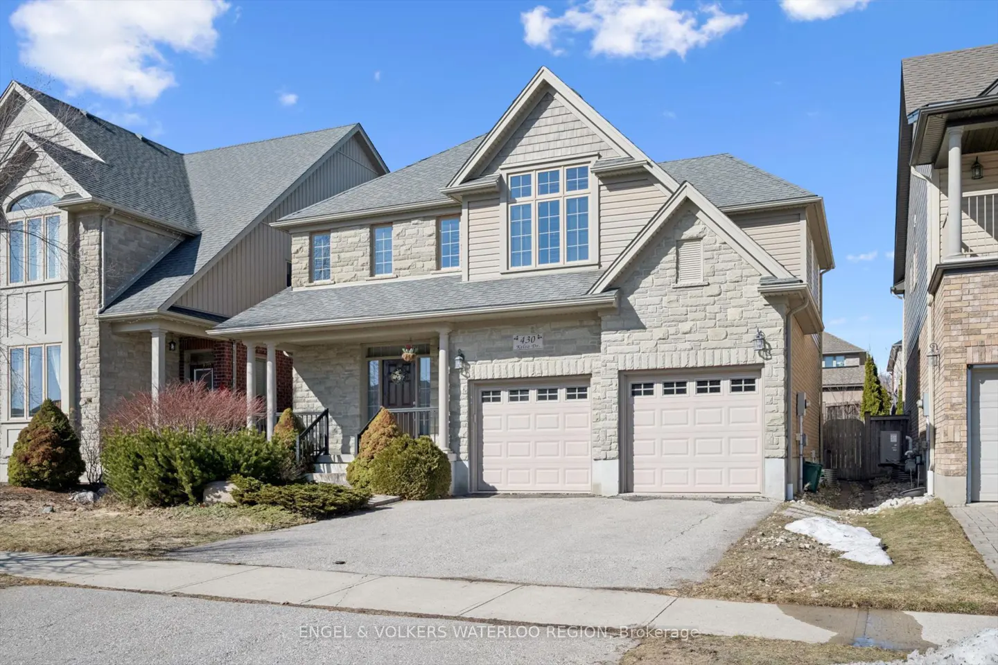 Two-story house with stone and beige siding, a gray roof, and a two-car garage on a sunny day.