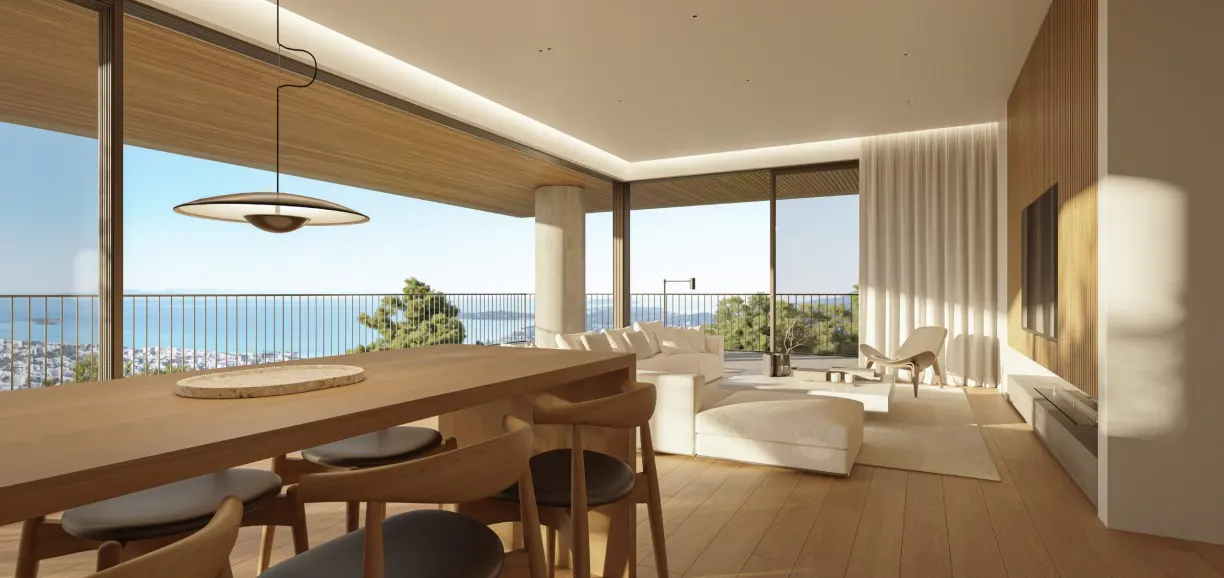 Bright, modern living space with wood floors, a long table with chairs, and a white sofa. Large windows offer a scenic ocean view.