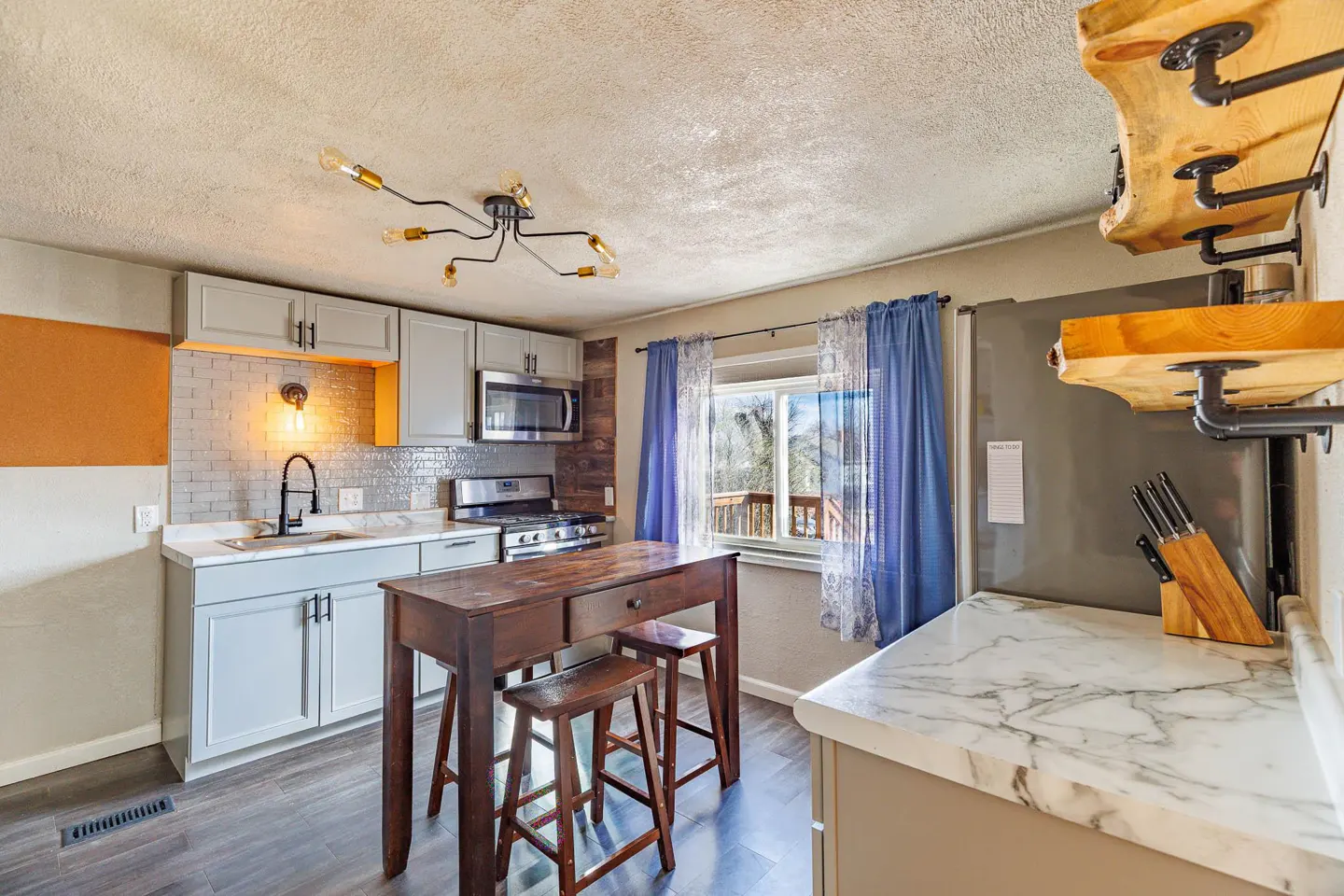 A kitchen with gray cabinets, a dark wood island with stools, and a window with blue curtains.