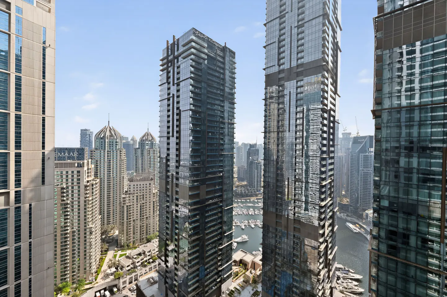 View of Dubai Marina with modern high-rise buildings and yachts docked in the harbor on a sunny day.