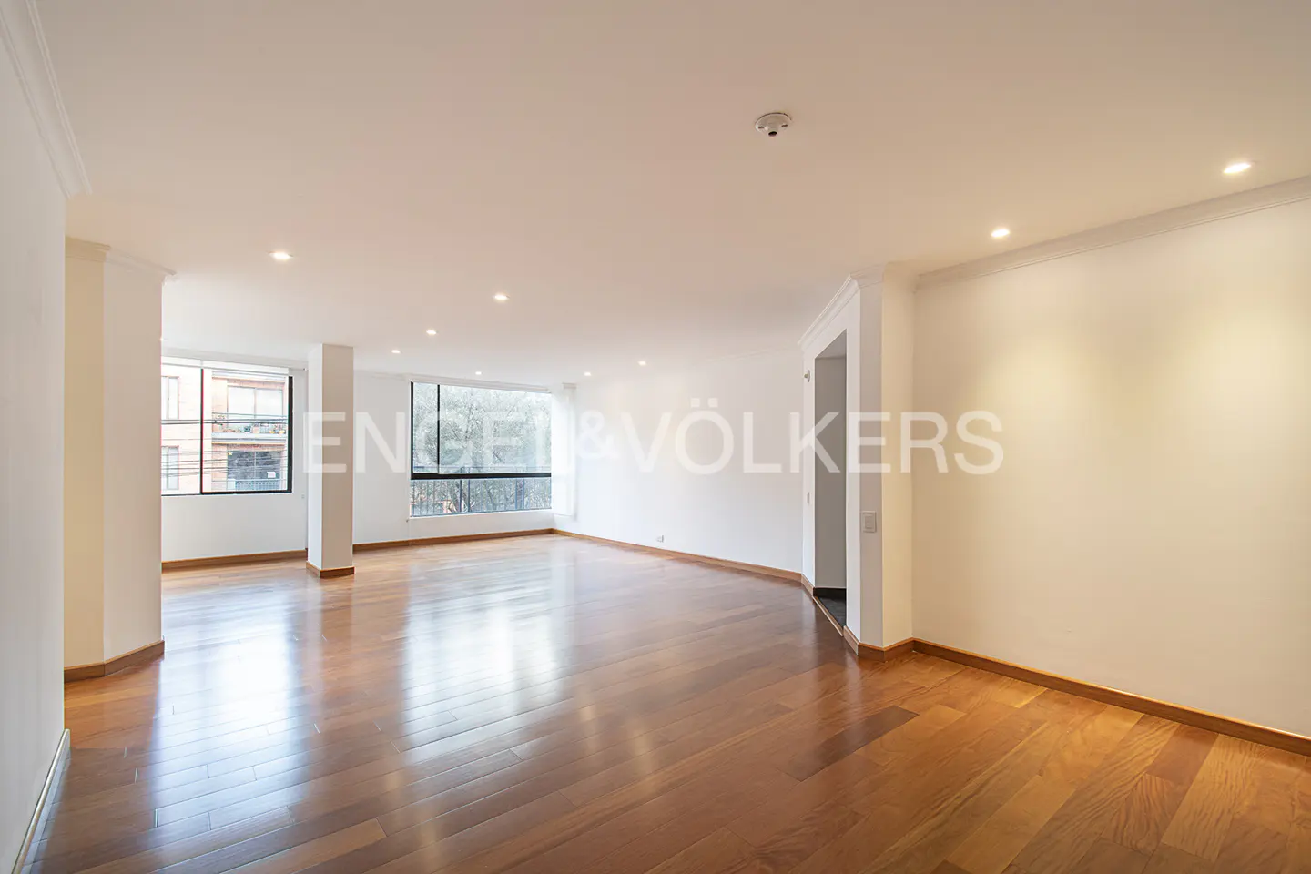 Empty room with hardwood floors, white walls, and large windows. Natural light fills the space. Engel & Völkers logo visible.