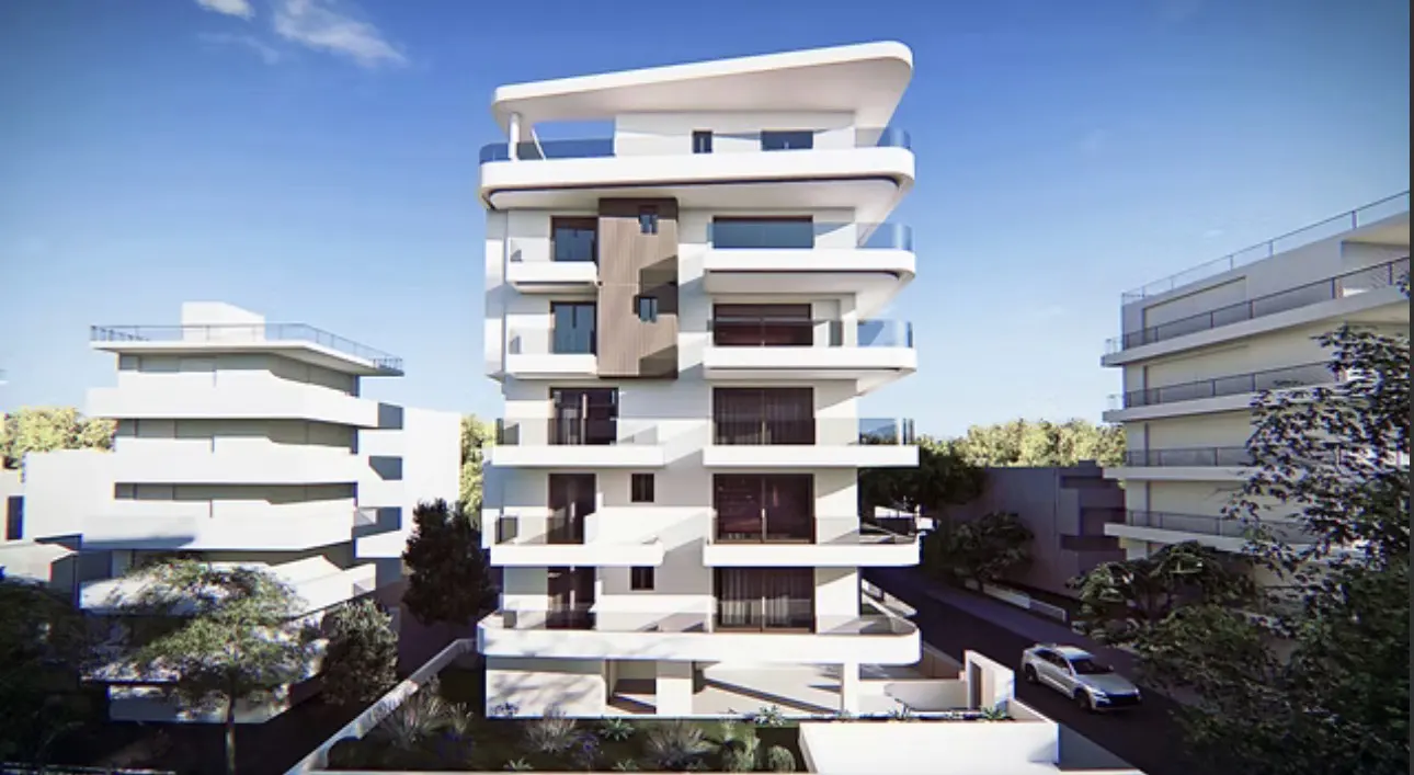 Modern white apartment building with glass balconies, set against a blue sky and green trees. A car is parked nearby.