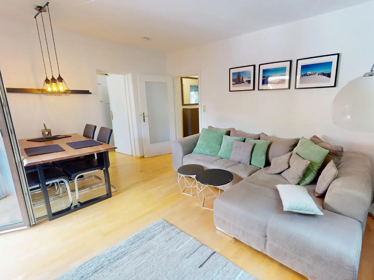 Living room with a dining table, a gray sofa with green pillows, and framed pictures on the wall.