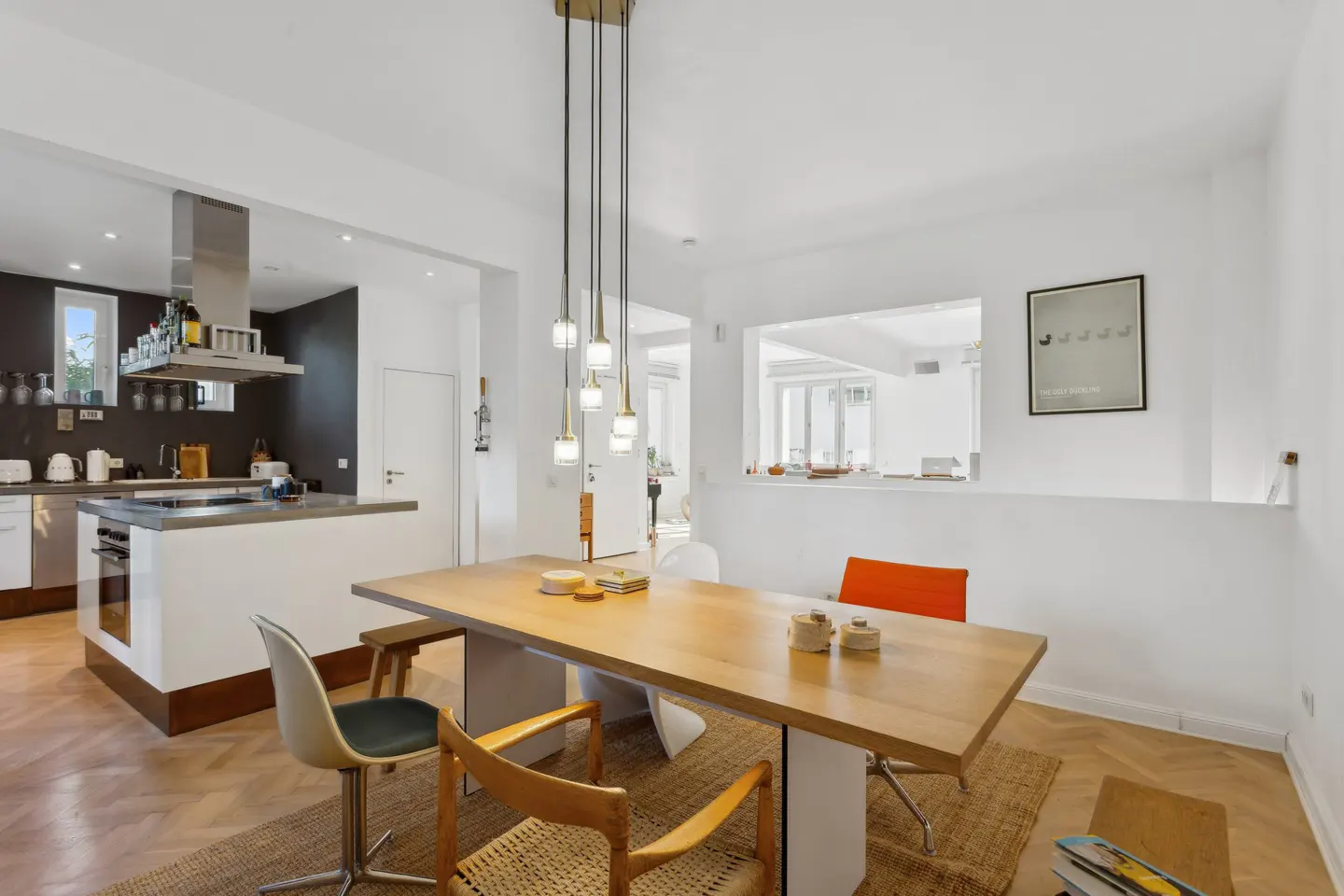 Bright, open-concept kitchen and dining area with a light wood table, modern pendant lighting, and white walls.