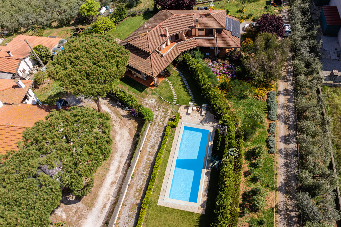 Aerial view of a terracotta-roofed house with a pool, surrounded by green trees and gardens.