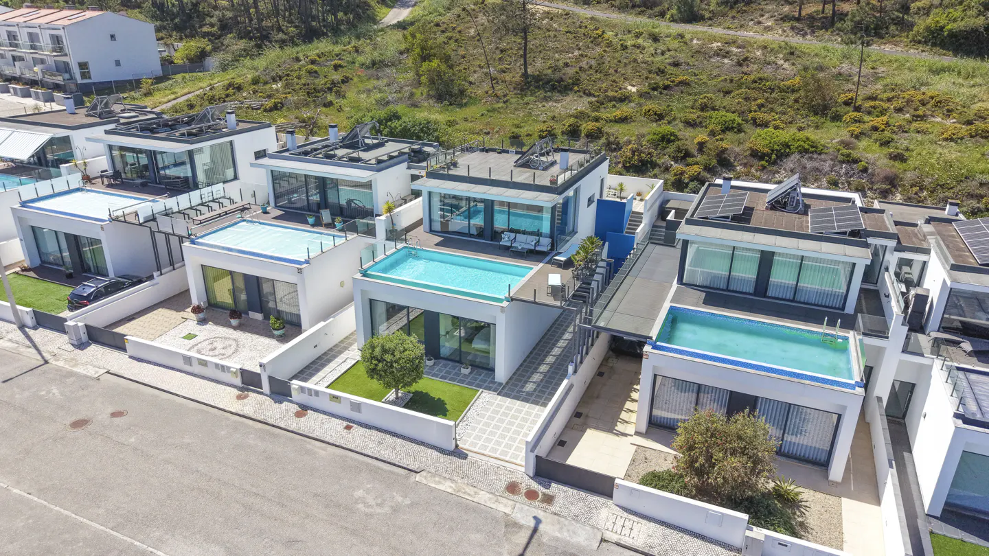 Aerial view of modern white houses with rooftop pools and solar panels, showcasing luxury real estate.