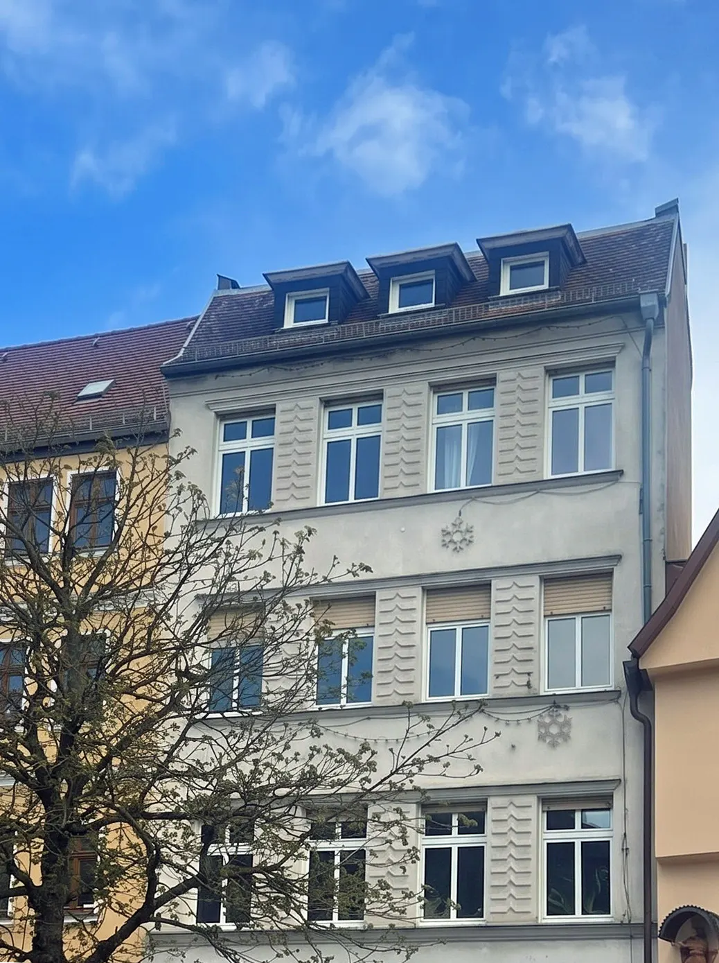 Four-story apartment building with white windows and dormers under a blue sky.