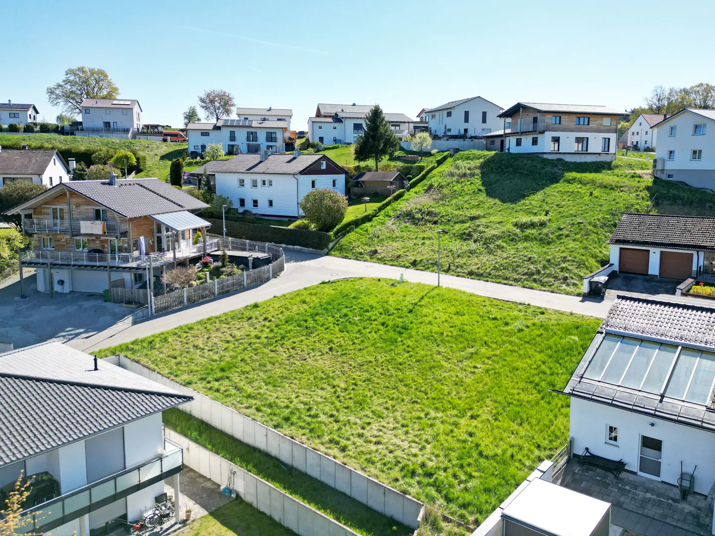 Aerial view of a grassy lot in a residential area with houses on a hill under a blue sky.