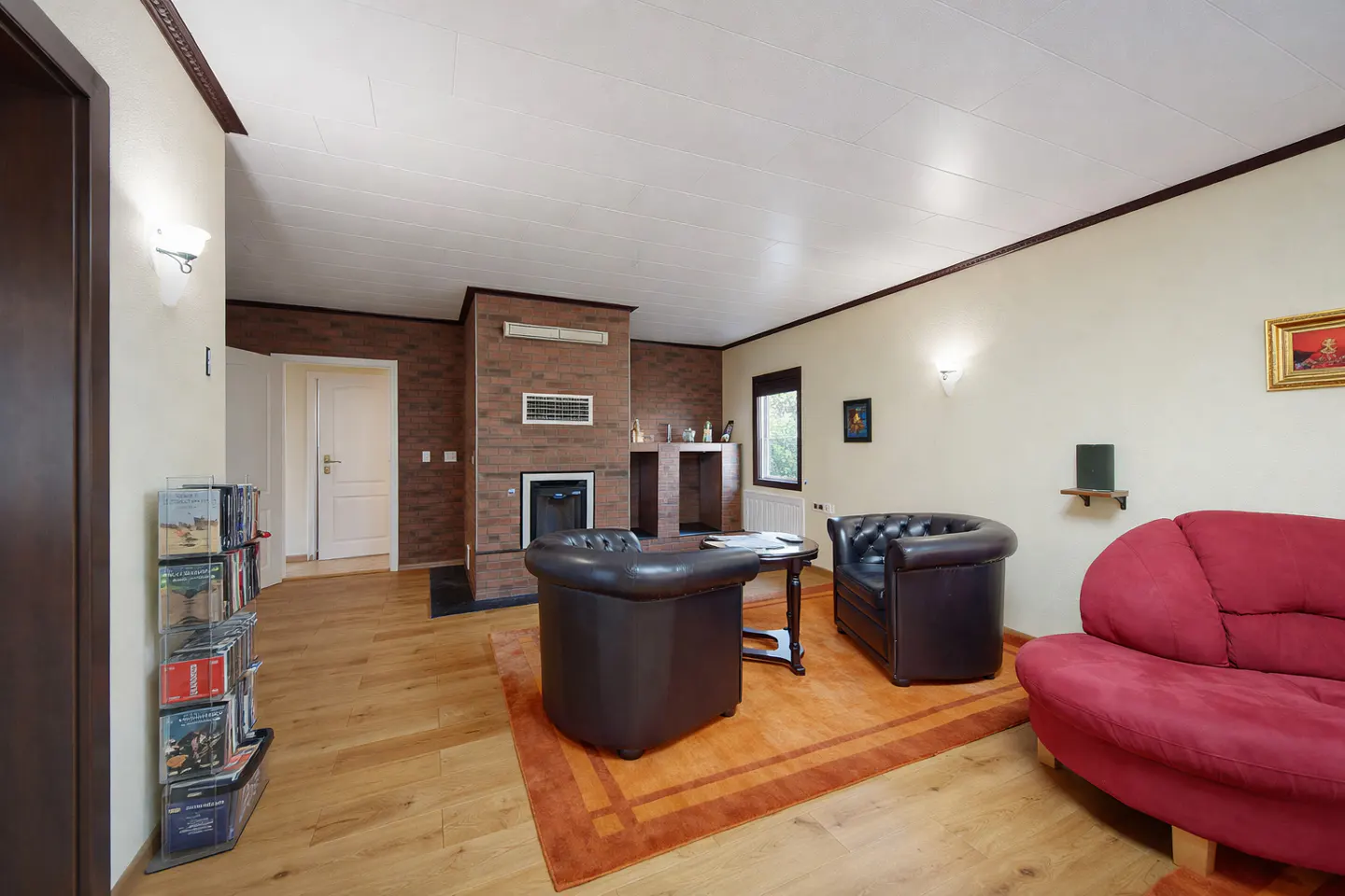 A living room with a red sofa, two brown leather chairs, and a brick fireplace.