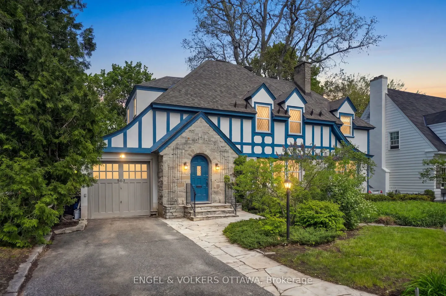 Exterior of a Tudor-style home with blue trim, stone accents, and a blue front door. A stone walkway leads to the entrance.