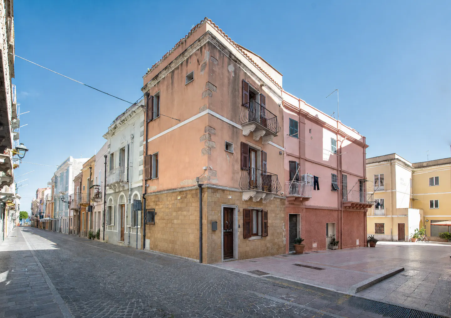 Street view of colorful buildings with balconies under a clear blue sky. Cobblestone street and sidewalks.