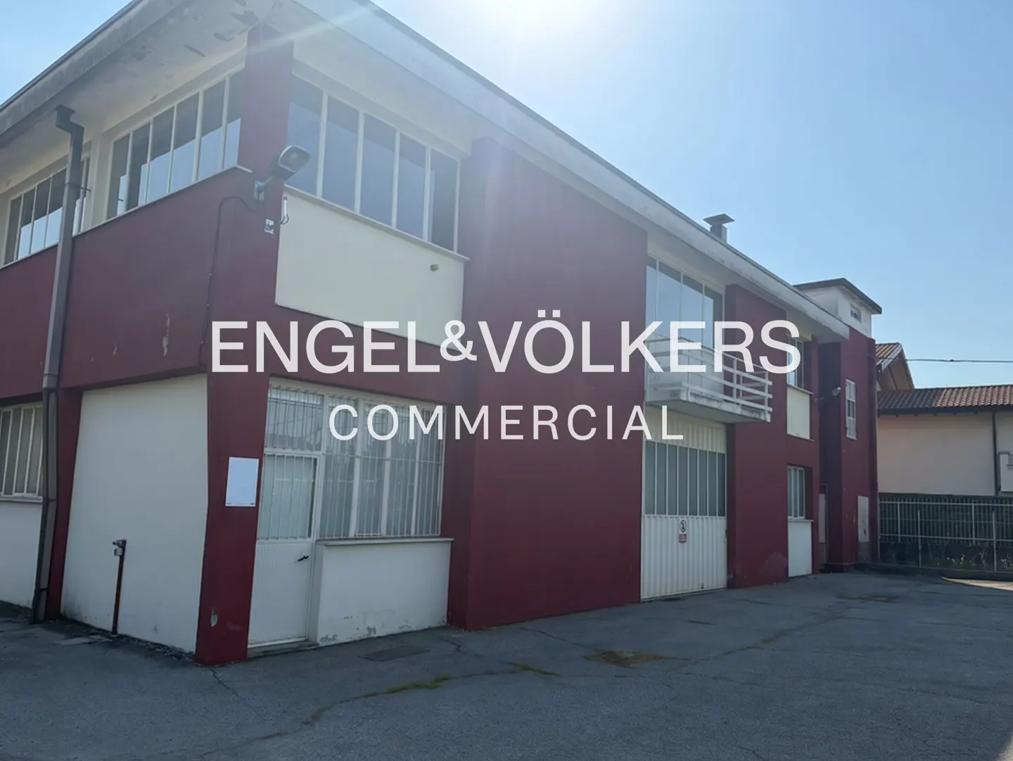 Two-story commercial building with red and white exterior, large windows, and Engel & Völkers Commercial logo.