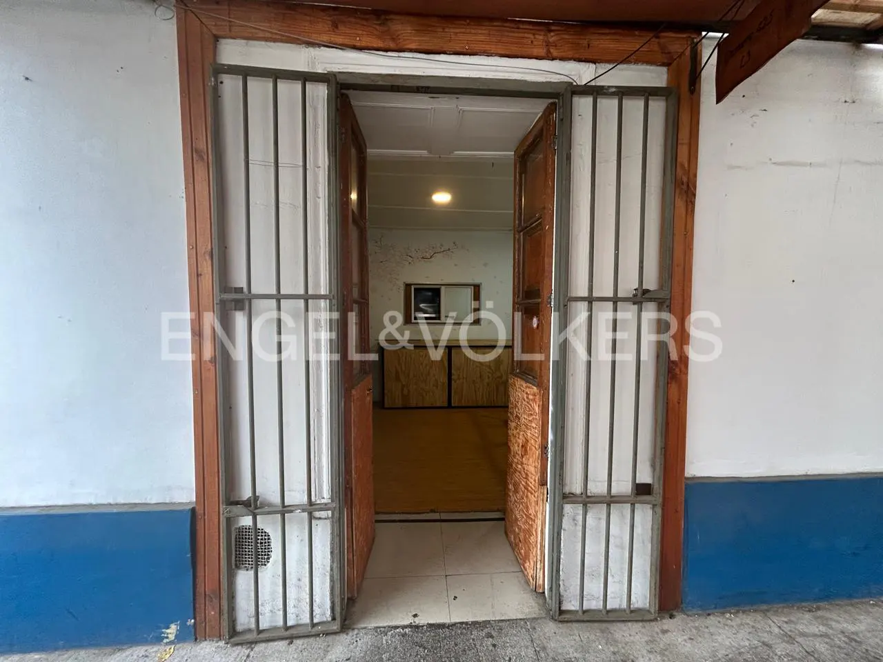 Open doorway with metal security gates leading into a dimly lit room with wooden counters and a single ceiling light.
