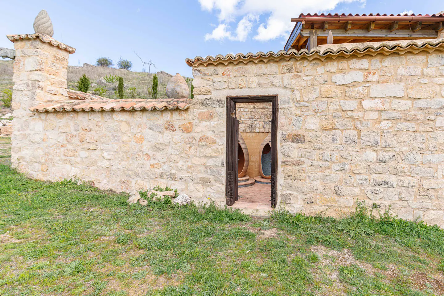 Exterior view of a stone building with a doorway leading to a courtyard with large pottery.