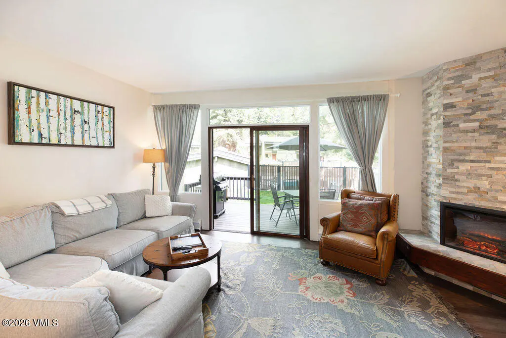 Living room with gray sofa, leather chair, stone fireplace, and sliding glass doors to a deck. A floral rug covers the floor.