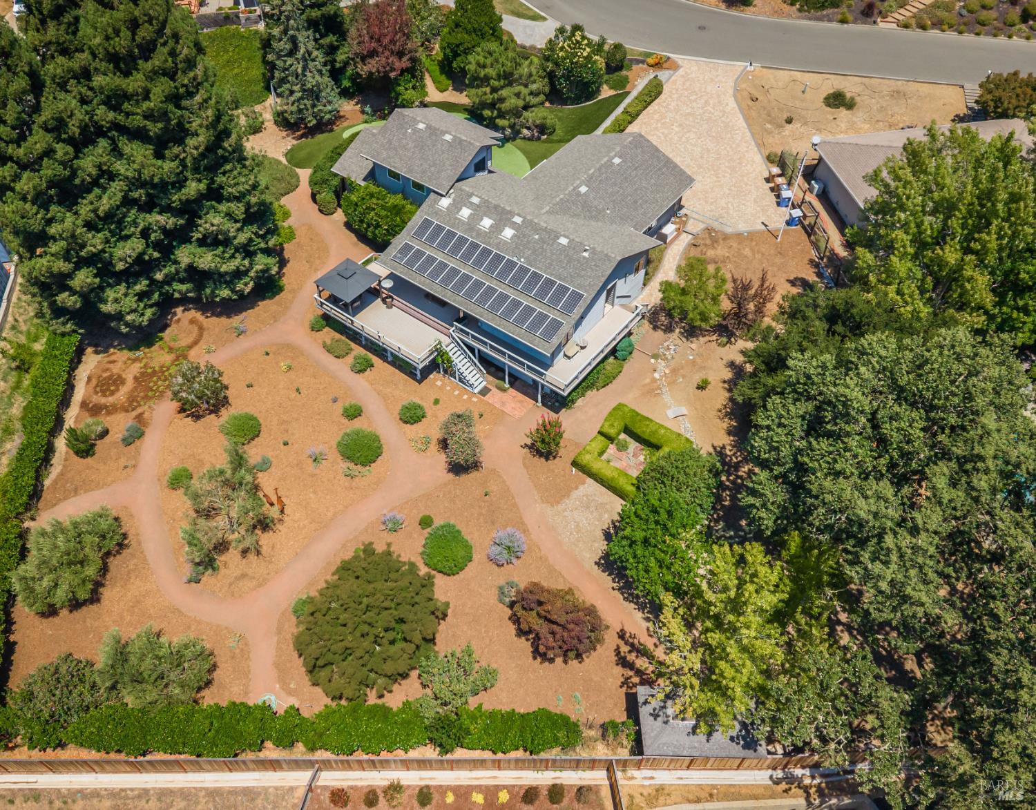 Aerial view of a house with solar panels, a large deck, and a landscaped yard with walking paths and mature trees.