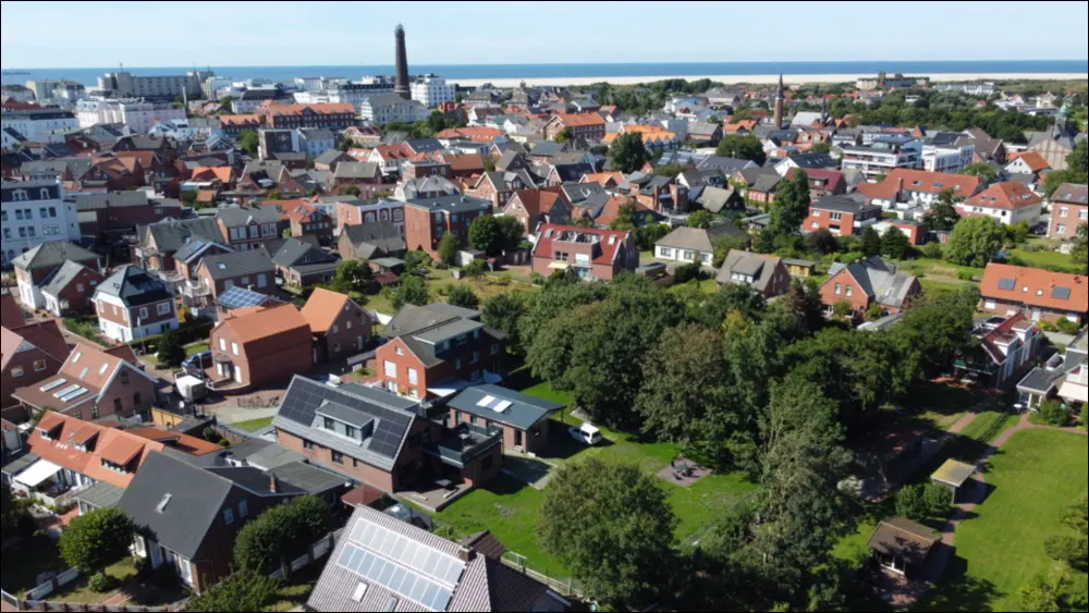 Aerial view of a coastal town with red-roofed houses, green trees, and the ocean in the background.