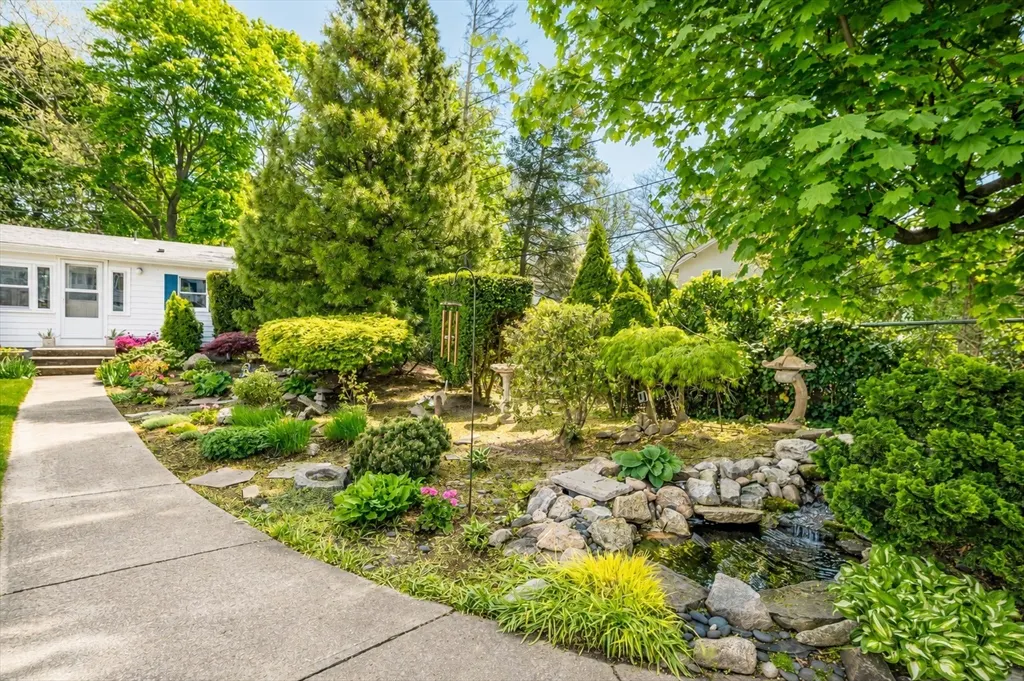 Landscaped front yard with a stone walkway leading to a white house with blue trim. A small stream flows through the garden.