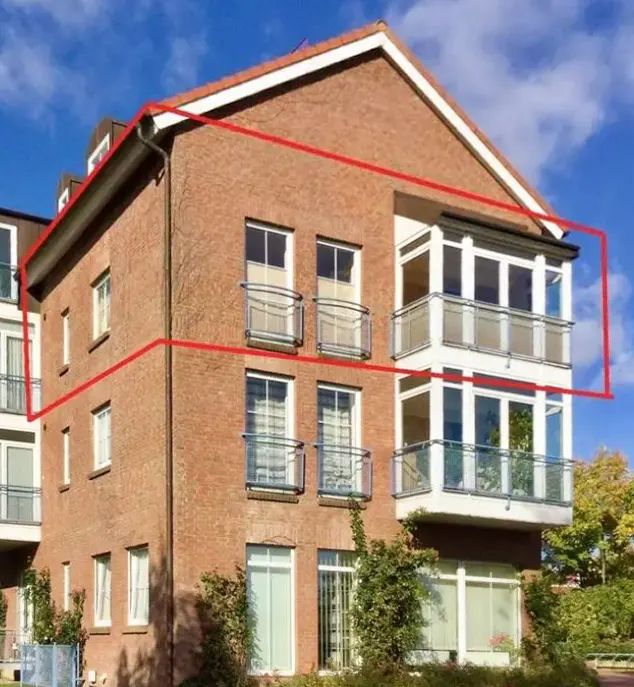 A three-story brick apartment building with white-framed windows and balconies. A red line highlights the building's perimeter.
