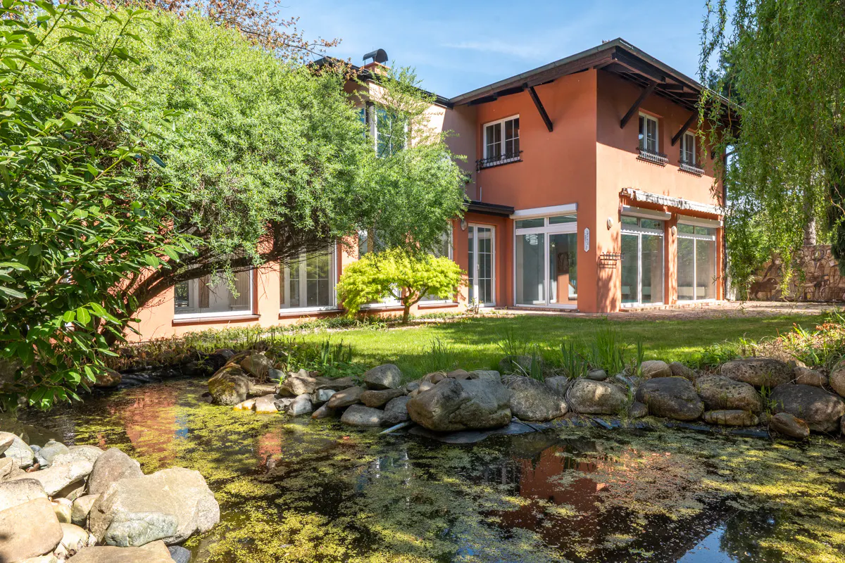 Exterior view of a two-story peach house with a pond and green lawn.
