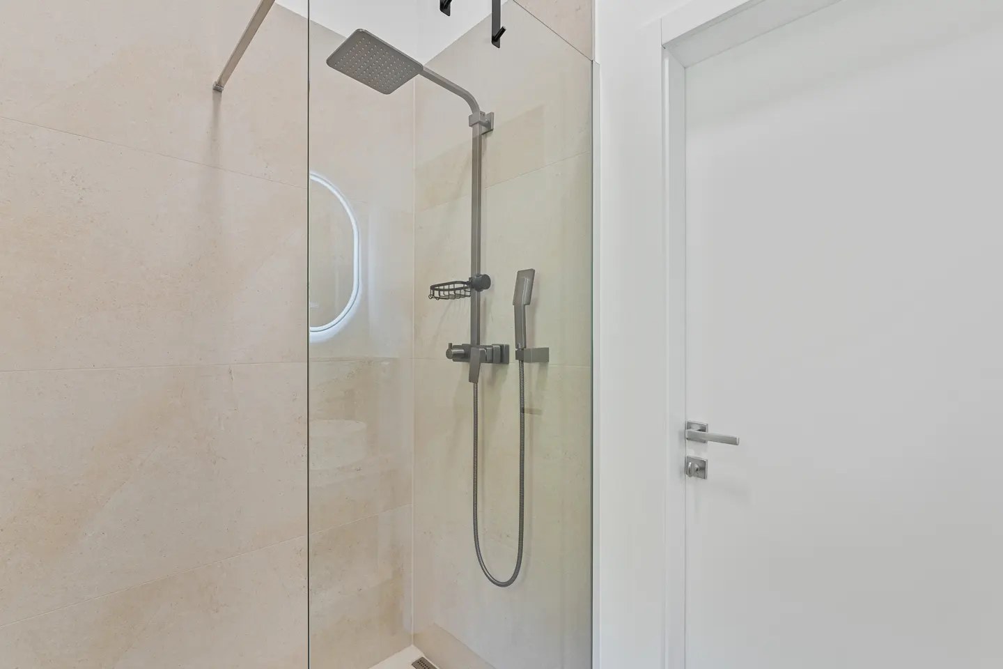 Modern bathroom with a glass-enclosed shower featuring a square showerhead, handheld sprayer, and a white door.