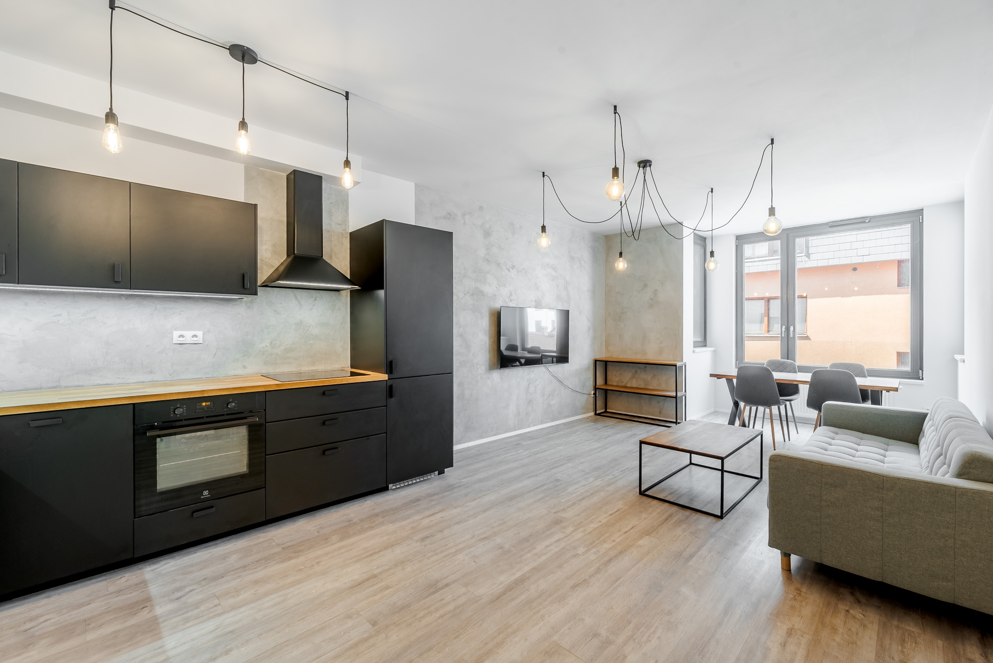Modern open-plan apartment with matte black kitchen cabinets, light wood floors, gray sofa, and industrial pendant lighting. [AI-generated text]