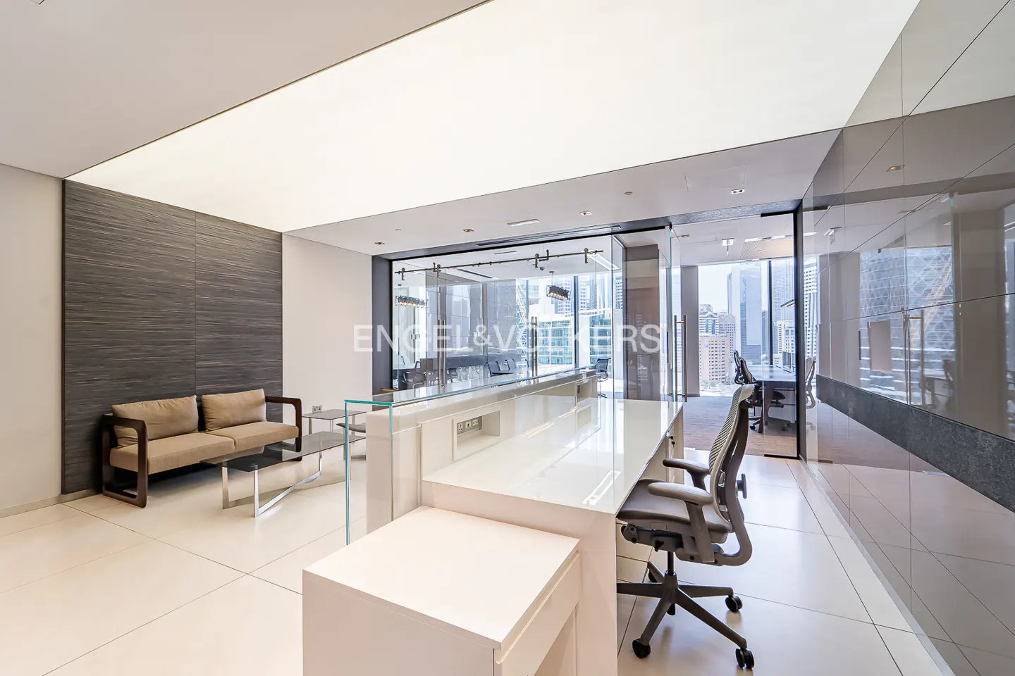 Modern office space with a white reception desk, gray office chair, and a tan sofa against a gray wall.
